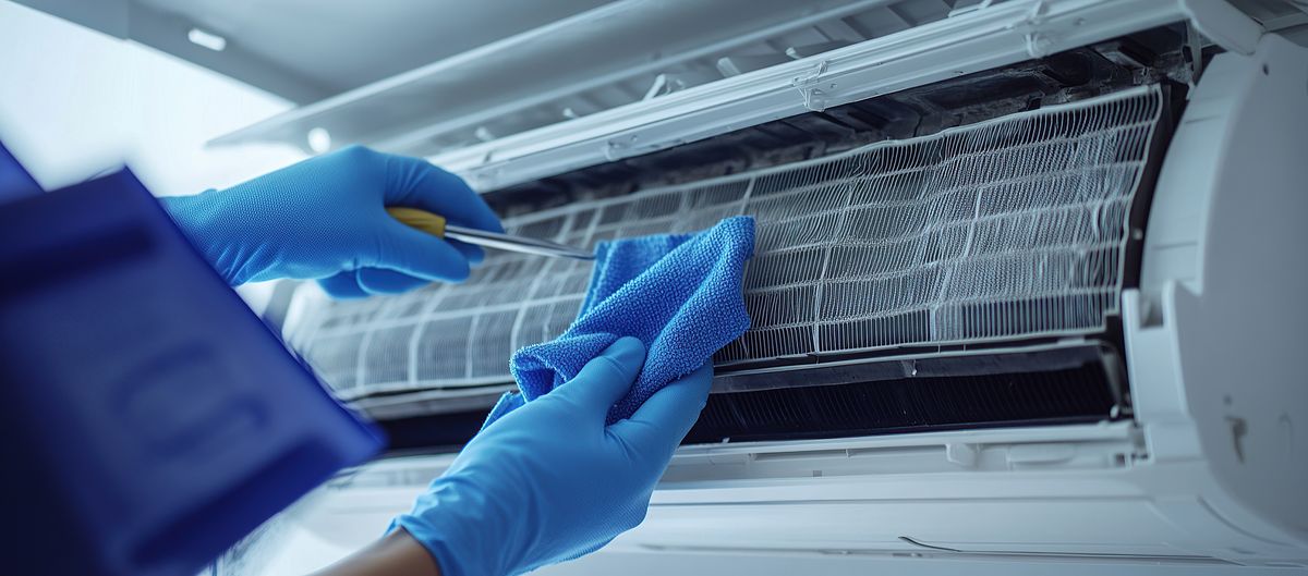 Monteur met handschoenen reinigt de warmtewisselaar van een binnenunit met een microvezeldoek